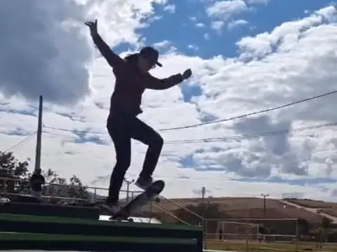 Skatista em silhueta fazendo manobra na escada de uma pista, com céu azul ao fundo.
